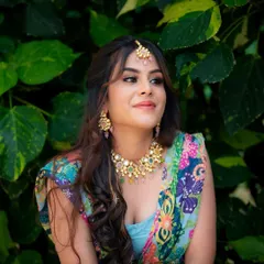 A candid, happy portrait against a dark green leafy background. The contrast makes the colors of her outfit and her bright smile pop.