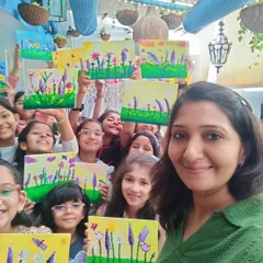 A group selfie with the birthday girl's mother and all the young guests at Nishka's 10th birthday party. Everyone is happily holding up their unique floral canvas paintings, showing the wonderful results of a creative party activity.