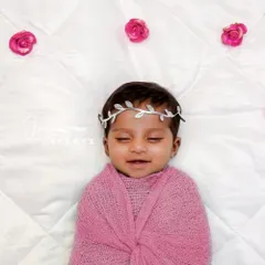 Simplicity at its finest. A newborn baby girl is swaddled in a soft pink wrap, wearing a delicate silver leaf headband on a clean white, quilted background. This pristine theme focuses entirely on your baby's peaceful expression.