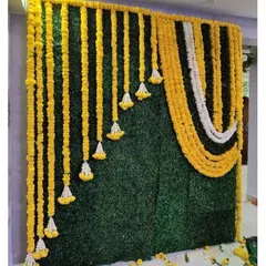 This backdrop uses a green grass wall as a base, beautifully contrasted with hanging garlands of yellow and white marigolds. It's a fresh and traditional look for a Haldi ceremony.