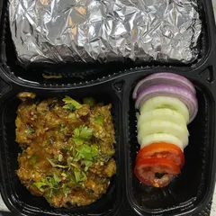 This tiffin features a home-style Baingan Bharta, a smoky roasted eggplant mash cooked with spices. It comes with fresh salad and rotis, offering a rustic and flavorful meal.