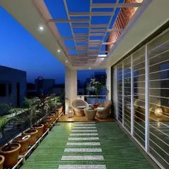 A long balcony beautifully lit for evening use. The overhead structure with integrated lighting and the path of stepping stones on the green floor guide you through the space, creating a serene and expansive feel at night.