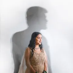 A creative and artistic portrait using shadow play. The silhouette of the groom is cast on the wall behind his beautifully dressed bride, symbolizing his presence and support. This is a unique concept for an engagement or pre-wedding shoot.