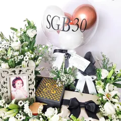 For a 30th birthday, I created this elegant black and white themed hamper. It includes a custom "SGB30" balloon, a beautiful photo frame to capture a special memory, and luxury essentials, all surrounded by fresh white lilies and roses for a sophisticated celebration.