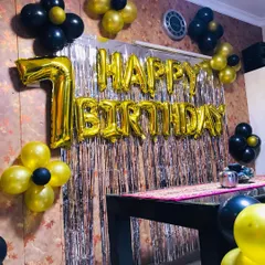 A simple yet festive 7th birthday setup. This decoration uses a silver foil curtain as a backdrop for a dining table, framed with black and gold balloon clusters and a large number "7" foil balloon.