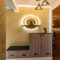This foyer unit creates a serene entrance with a backlit circular niche for a small statue. The design includes a shoe cabinet with a seating bench, combining spiritual and practical elements.