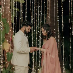 The ring exchange moment during an intimate engagement ceremony, set against a curtain of warm fairy lights.