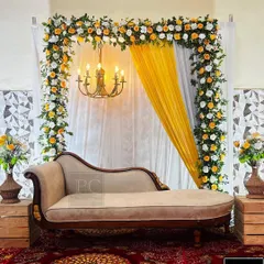 A classic and regal setup for a ring ceremony. The decor features a beautiful floral arch of white and yellow roses, a vintage-style chaise lounge, and a chandelier for a touch of royalty.