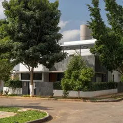 The home as seen from the street corner, nestled among mature trees. The design uses a combination of white plaster and dark slate cladding to create a visually interesting and modern facade.