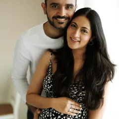 A classic portrait of a smiling, happy couple, taken with soft, natural light in their home. His arms are wrapped around her, sharing their joy with the world.