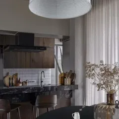 The kitchen and dining area in this apartment are defined by a rich material palette, including dark marble, wood cabinetry, and a dramatic paper lantern.