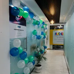 A balloon garland in shades of blue, green, and white, arranged along the glass wall of an office for a celebration.