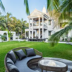 A daytime view of the circular deck at 'Tropical Manor'. The space is designed for tranquility, surrounded by a lush lawn and framed by the modern gothic architecture of the villa, creating an immersive connection with nature.
