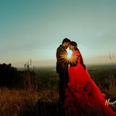 A beautiful sunset silhouette of a couple about to kiss, with a starburst effect from the setting sun. The bride's red gown adds a touch of color to the dramatic landscape.