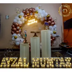 We personalize your celebration with light-up marquee letters for a truly custom touch. This beautiful rose gold and white balloon arch is the perfect frame for the birthday person's name, set against a simple wall for a clean, sophisticated look.