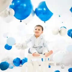 A classic first birthday portrait. This little boy sits proudly on a "ONE" prop, surrounded by a sea of blue and white balloons, creating a clean and celebratory image.
