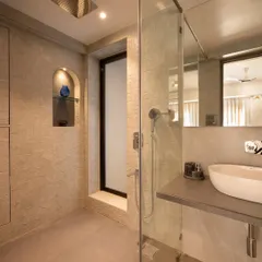 This master bathroom features textured beige tiles and a floating concrete-finish countertop. The arched niche in the shower area adds a soft architectural detail and practical storage for toiletries.