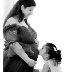 A heartwarming black and white photo capturing a tender moment between a mother-to-be and her daughter, who is kissing the baby bump. We love including siblings to make it a full family celebration.