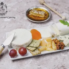 An elegant display of fine cheeses, perfect for an intimate gathering. This platter features a wheel of soft Brie, piquant blue cheese, and goat cheese, beautifully paired with crackers, grapes, dried apricots, walnuts, and a dish of pure honeycomb.