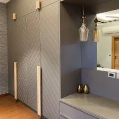 A detail of a grey wardrobe with a chevron pattern and light wood handles. A small dresser nook with a mirror and pendant lights is seamlessly integrated into the design.