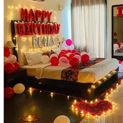 I love making birthdays personal. This decoration features custom name balloons ("RENA"), a pathway of LED candles leading to the bed, and a heart shape made from fresh rose petals for a truly bespoke surprise.