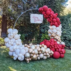 An elegant circular balloon arrangement for a garden party. The red, white, and gold balloons create a beautiful contrast with the natural green background.