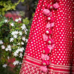 A detailed shot of the tassels on a bride's red lehenga, set against a backdrop of white flowers. It's the small details that make the outfit.