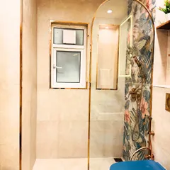 A stylish bathroom with a unique arched glass shower partition framed in gold. The tropical-print accent wall inside the shower adds a vibrant and unexpected design element.