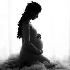 A serene and beautiful silhouette portrait of a mom-to-be. The soft light and the texture of the ruffled gown create a stunning monochrome image.