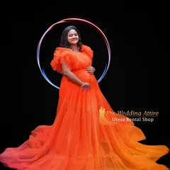 This bright orange ruffled gown is perfect for a modern and vibrant studio maternity shoot. The voluminous tulle skirt and ruffled shoulders create a high-fashion look against a simple black background.