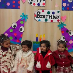 Four little friends stand together in front of a colorful birthday backdrop, celebrating a classmate's special day. These moments help build early friendships.