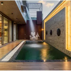 We design spaces that extend living beyond the walls. This tranquil poolside area features a custom water curtain cascading from the balcony above, creating both a visual centerpiece and a soothing auditory experience. The combination of dark water, warm deck lighting, and textured concrete walls makes this a perfect retreat for relaxation or evening entertainment.