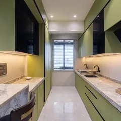 This angle highlights the parallel counter layout of the Kalyan kitchen, providing ample workspace. The design incorporates black matte fixtures and profile handles for a sharp, contemporary contrast against the green cabinets.
