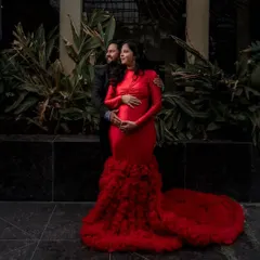 This dramatic red mermaid gown features a full, ruffled tulle train, combining a sleek silhouette with a touch of theatrical flair. It's a perfect choice for a glamorous evening-style maternity shoot.