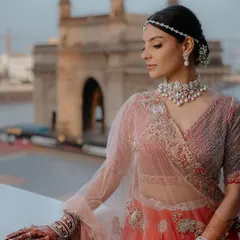 A modern take on the red bridal look, set against the iconic Gateway of India. Her makeup is clean and elegant, with a focus on radiant skin and a simple bindi, letting her natural beauty and the stunning view shine.
