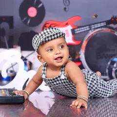 A happy baby crawls across the floor in a music-themed setup, full of energy and joy. The checkered outfit and matching cap complete his rockstar look.