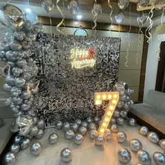 A glamorous 7th-anniversary celebration featuring a floor-to-ceiling silver sequin backdrop, a neon sign, and a large illuminated number '7'.