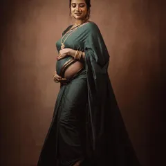 A full-length maternity portrait with a vintage, painted feel, showcasing the mother-to-be cradling her belly in a beautiful green saree.