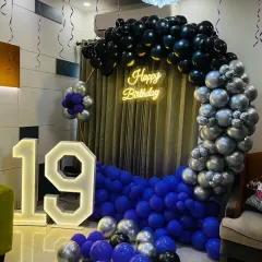 I can match any theme, including this cool and stylish 19th birthday party. The decoration features a moody color palette of purple, black, and silver balloons, a 'Happy Birthday' neon sign, and a large light-up marquee number '19'.
