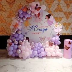 A lovely butterfly and fairy themed backdrop for a 5th birthday. The custom printed backdrop is framed by a beautiful arch of purple, pink, and silver balloons.