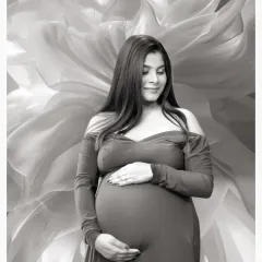 A serene black and white solo portrait of a mother-to-be cradling her bump, set against a soft, abstract floral background.