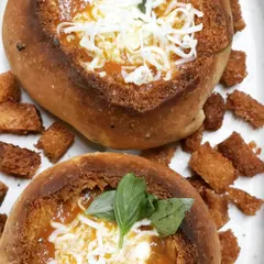A unique way to serve soup, these are our homemade bread bowls filled with a hearty tomato soup and topped with grated cheese. The bowl itself is edible, making for a fun and rustic meal.