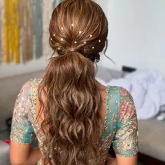 A chic and modern messy ponytail. This hairstyle is elevated with delicate pearl accents scattered throughout, making it perfect for a sangeet or reception.