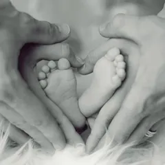 A classic and heartwarming newborn detail shot. Parents' hands form a heart shape around their baby's tiny feet, symbolizing the love and protection surrounding their new arrival.