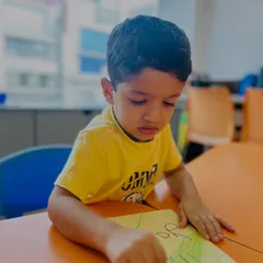 A boy points to his drawing, perhaps explaining his creation. Our classes encourage children to talk about their work, building their narrative skills.