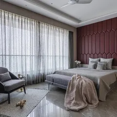 A bedroom in the 'Aria Residence' featuring a bold, geometric headboard in a deep red. This is balanced by neutral grey flooring and wardrobes with an interesting veneer pattern, creating a space that is both luxurious and modern.