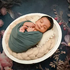 A striking portrait using a dark, moody floral backdrop. The contrast makes the peacefully sleeping baby, swaddled in teal, the clear focus of the image.