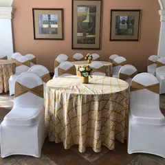 A clean and elegant seating arrangement for guests. We used round tables with patterned cloths, white chair covers with golden sashes, and simple floral centerpieces for a classic look.