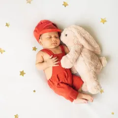 Dressed in a cute red outfit and snuggled up with a soft bunny, this newborn is ready for a nap under a sky of golden stars.