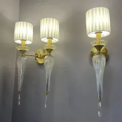 This pair of wall lights combines several classic elements: pleated fabric shades, ribbed glass bodies, and delicate crystal drops. The design is intricate and luxurious, perfect for adding a layer of texture and refinement.